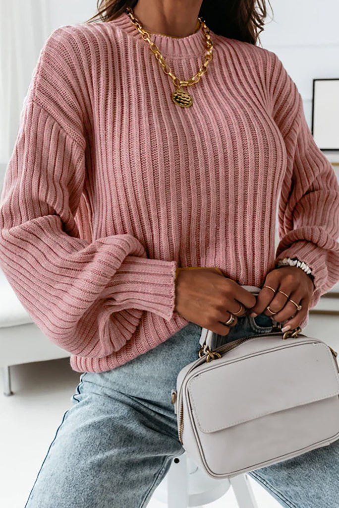 Woman wearing rose colored pink ribbed loose fitting sweater with light bnlue jeans